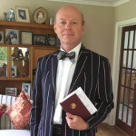Man wearing jacket and bow tie holding a book in formal sitting room